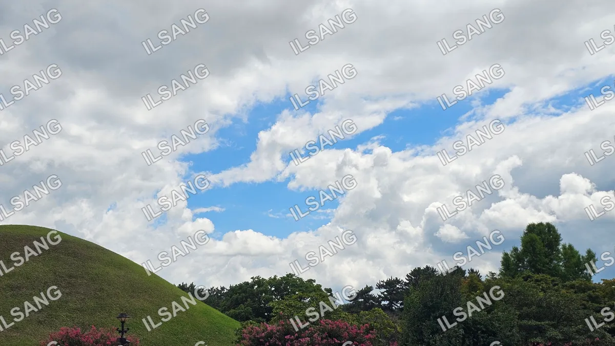 A beautiful blue sky with clouds and a green hillside.