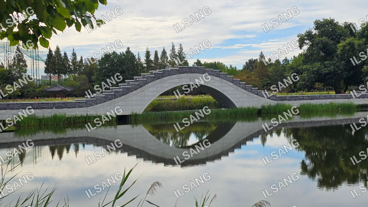 A bridge over a pond with a reflection of the bridge in the water.