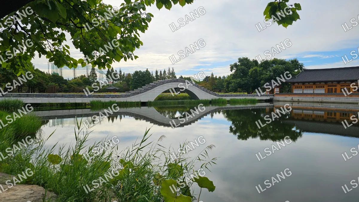 A bridge over a pond with a reflection of the bridge in the water.