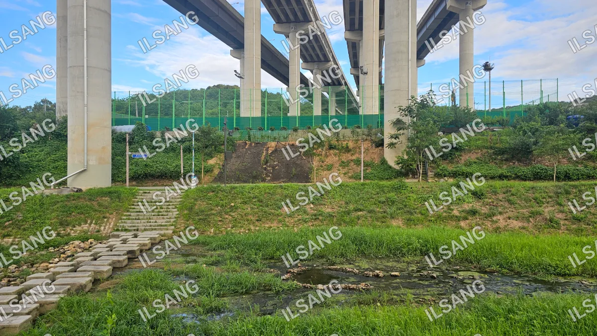 A bridge over a river with a green field and a small waterfall.