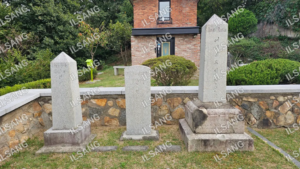 A cemetery with three gravestones and a brick wall.