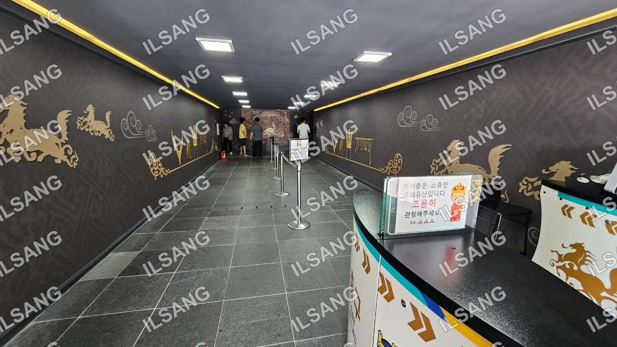 A group of people are standing in a long hallway with a metal barrier in front of them.