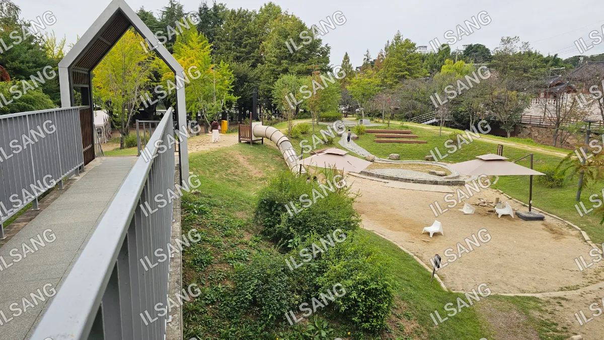 A park with a playground and a dog walking on a path.