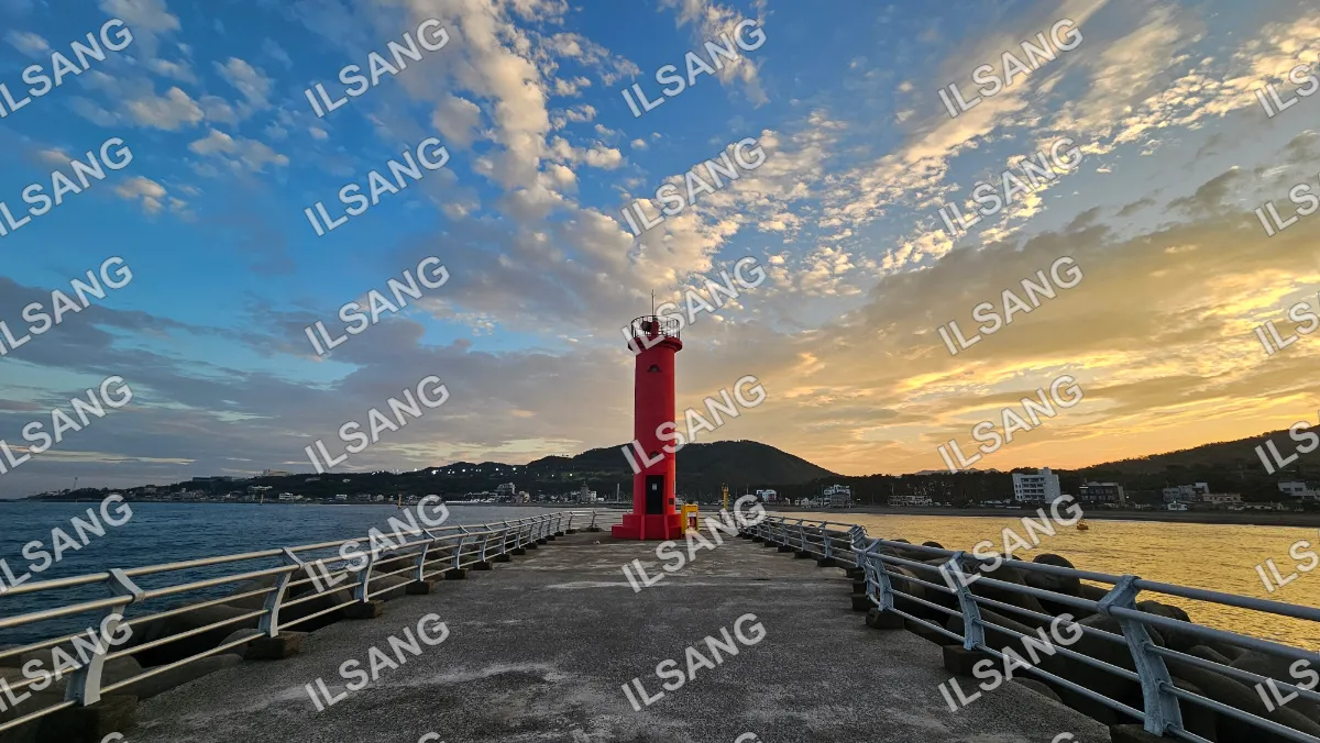 A red lighthouse stands on a dock in front of a cloudy sky.