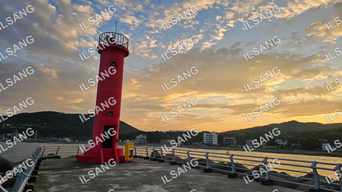 A red lighthouse with a yellow door and a white building in the background.
