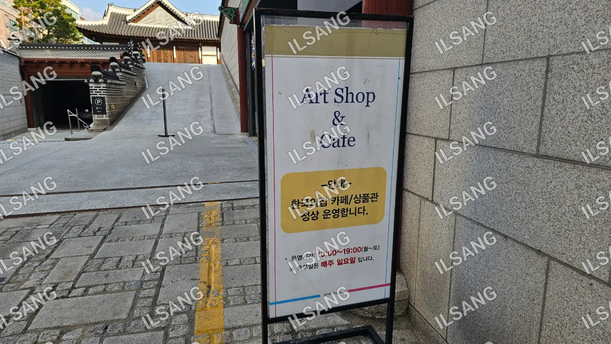 A sign for an art shop and cafe is posted on a stone wall.