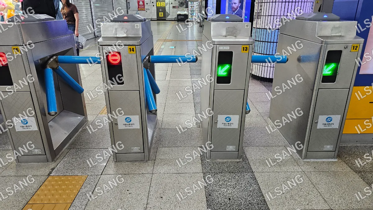 A silver subway turnstile with a green light on the bottom.