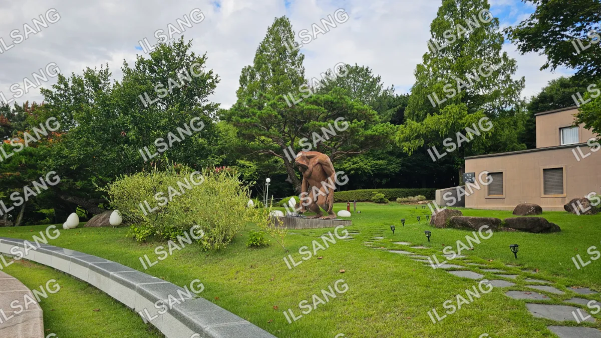 A statue of a man sitting on a rock is located in a park.