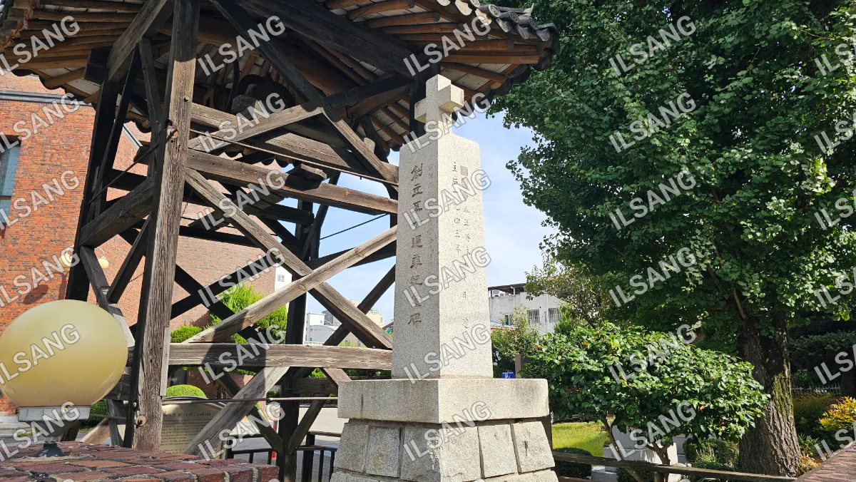 A stone monument with a cross on top is located in a park.