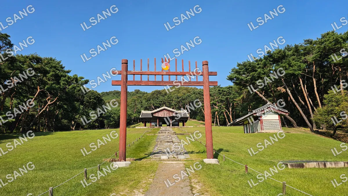 A wooden structure with a roof and a small building in the background.