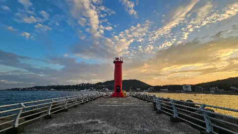 A red lighthouse stands on a dock in front of