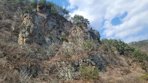 A rocky hillside with trees and a blue sky